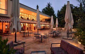 An outdoor seating area with tables and chairs, umbrellas, and a building with large windows in the background. - Nice apartment in Biograd with sauna (Biograd)