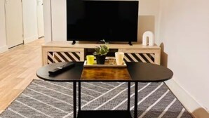 A modern living room with a flat-screen TV, a coffee table with a plant, and a remote control on the floor.