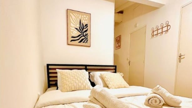 A neatly made bed with a headboard, a framed artwork on the wall, and a door with a decorative handle.