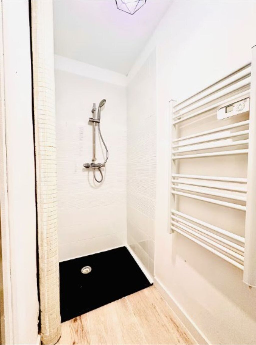 Een kleine badkamer met witte wanden, een douche, een zwarte mat en een handdoekhouder.