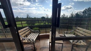 Un balcon doté de deux bancs en bois et d’une rambarde en métal, offrant une vue sur un paysage verdoyant.