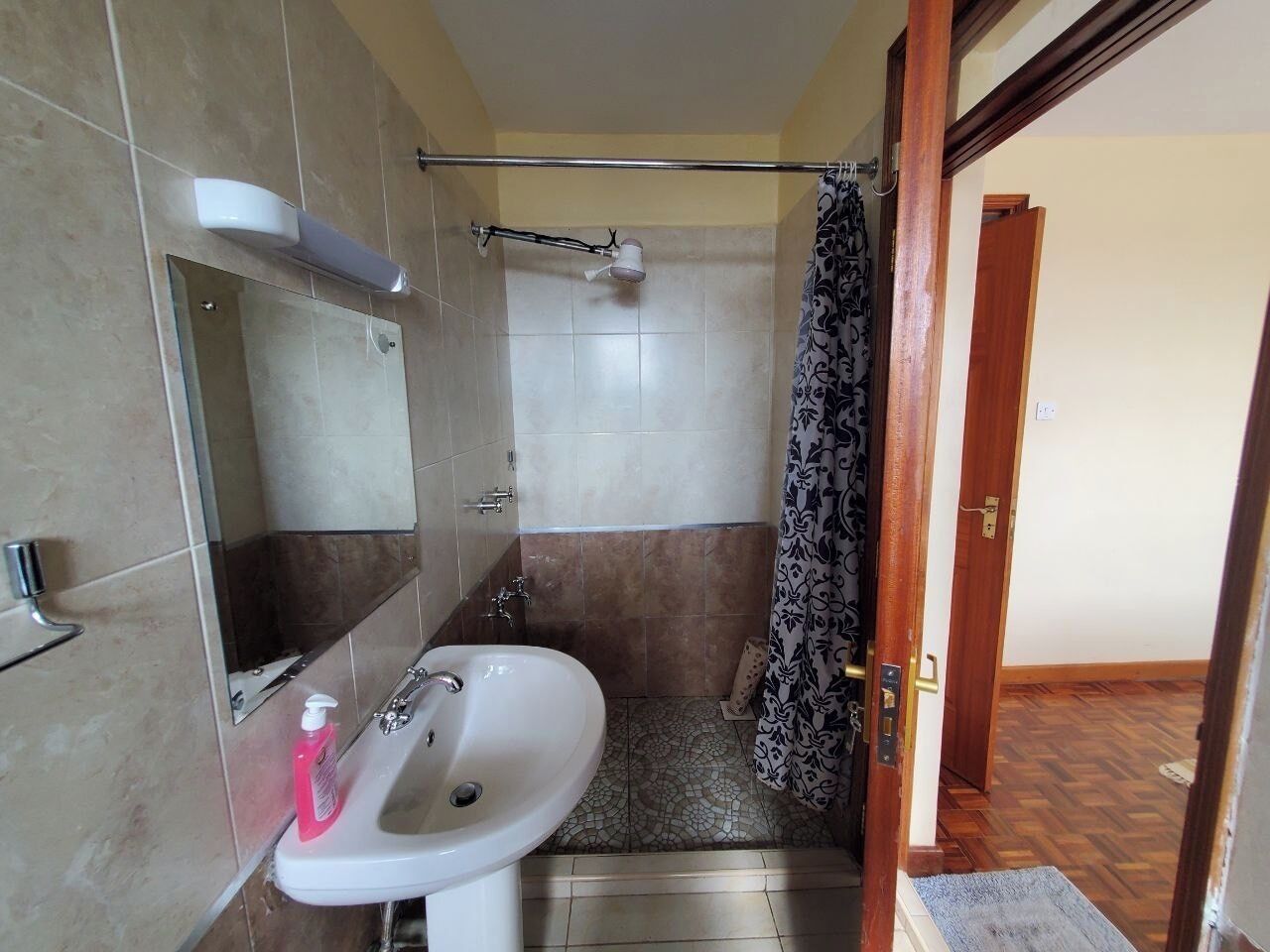 A bathroom with a sink, mirror, shower, and a door leading to another room.