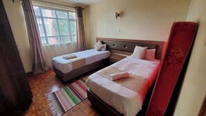 Une chambre d’hôtel avec deux lits, une fenêtre avec des rideaux, un plancher en bois et un tapis à rayures.