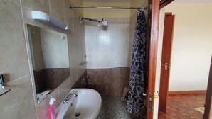 Une salle de bain équipée d’un lavabo, d’un miroir, d’une douche et d’une porte donnant sur une autre pièce.