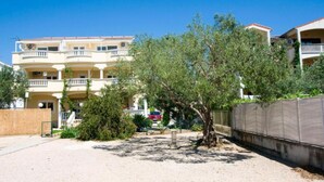 A multi-story residential building with balconies, a sandy ground, and a tree in the foreground. - Mobile homes Bella vita 2 (Biograd na Moru)