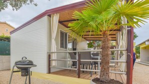 A small, single-story building with a covered porch, a grill, and a potted palm tree. - Mobile homes Bella vita 3 (Biograd na Moru)