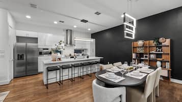 Una cocina moderna con armarios blancos, electrodomésticos de acero inoxidable y una isla central con taburetes de bar.