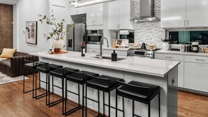Cozinha moderna com armários brancos, uma ilha grande com banquetas, eletrodomésticos de aço inoxidável e uma janela ampla.
