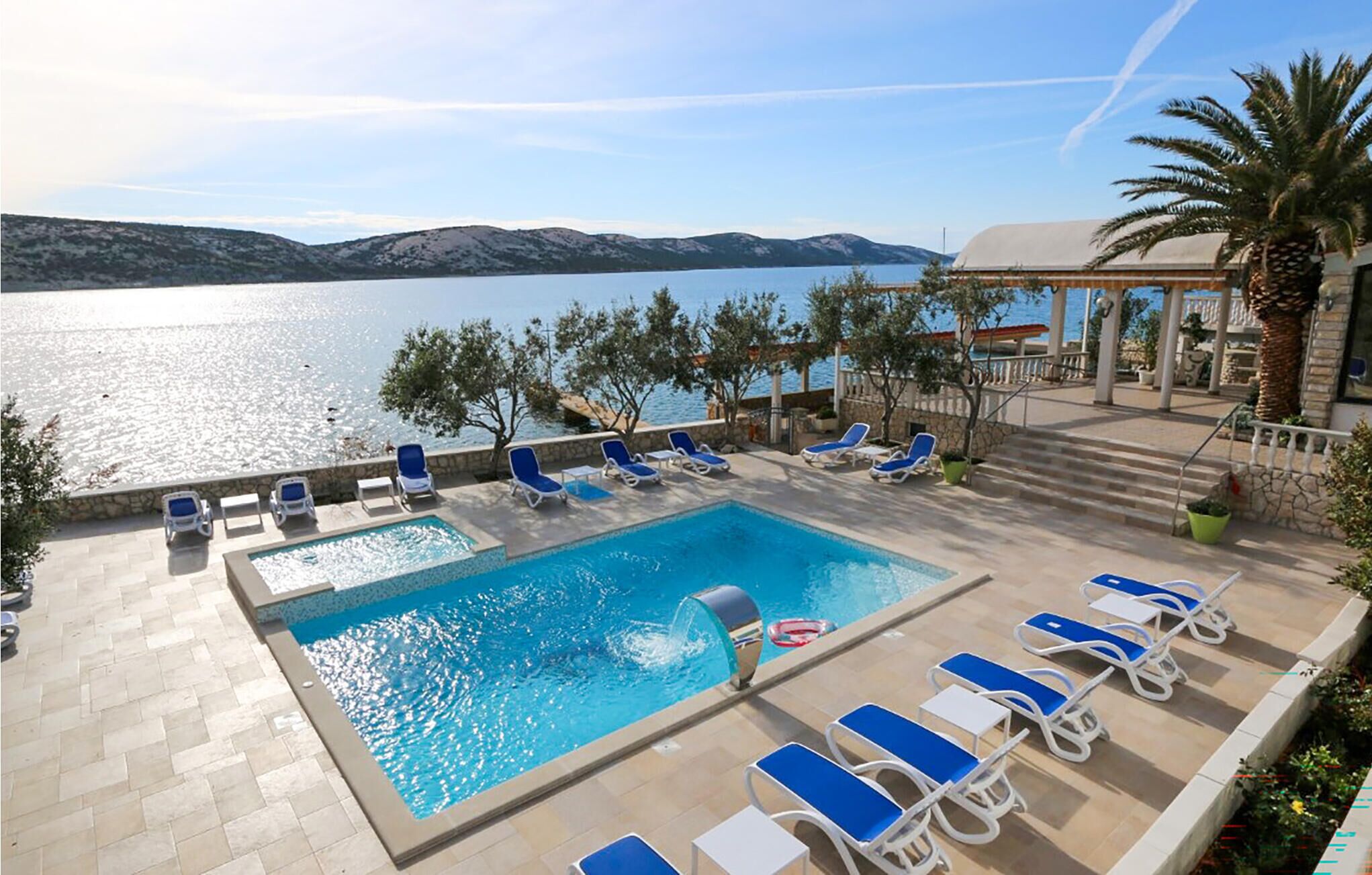 A pool area with blue lounge chairs and a view of the sea.