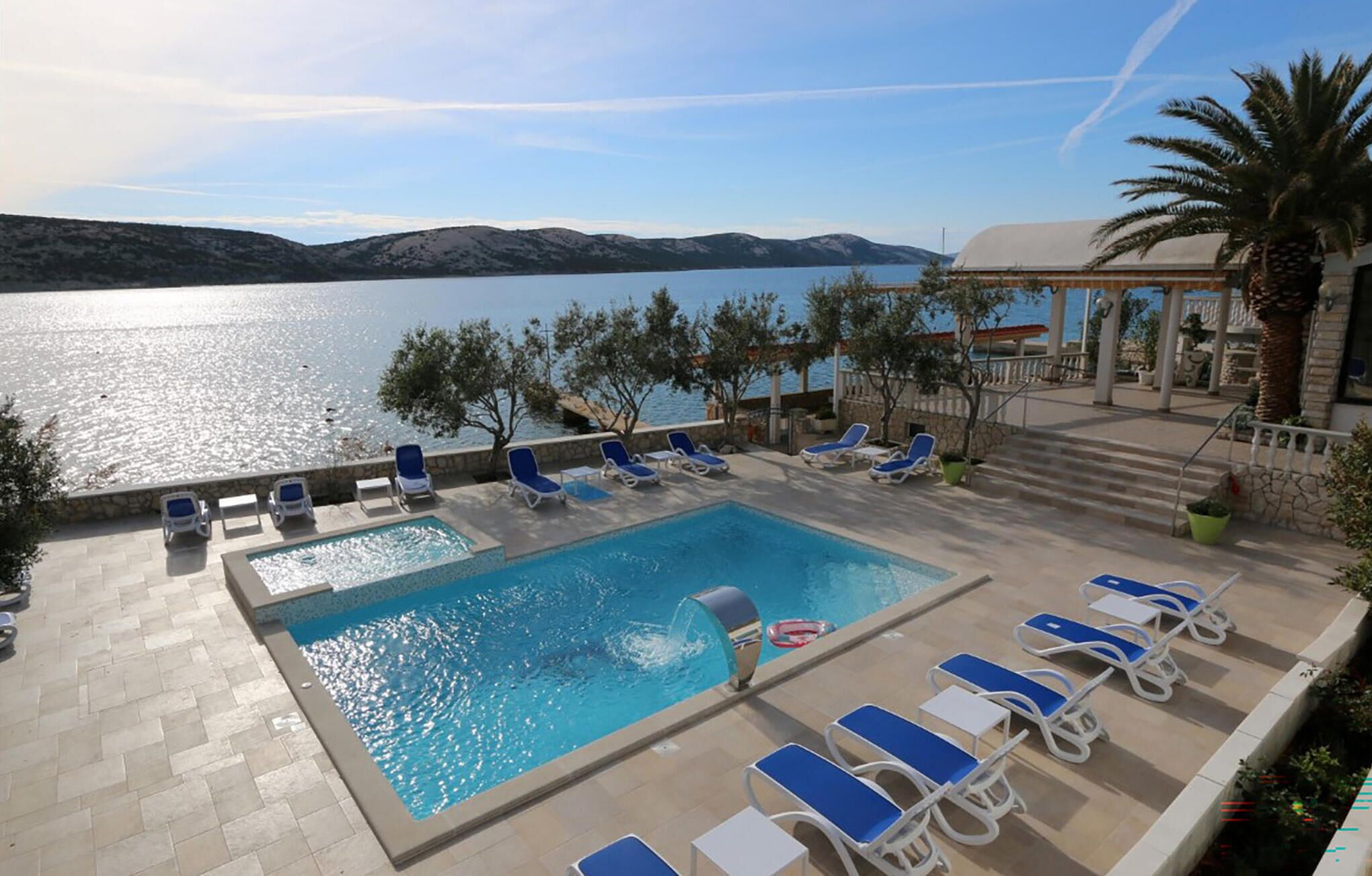 Un área de piscina con vistas al mar, sillas de descanso y un edificio al fondo.
