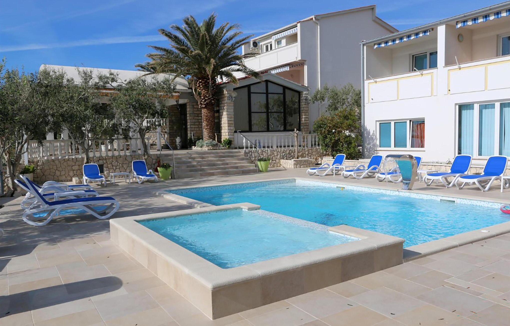 Ein Swimmingpool mit Liegestühlen, einer Steinmauer und einem Gebäude mit Balkon.