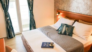 Een hotelkamer met een bed, nachtkastje, boek en raam met gordijnen.