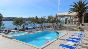 A pool area with two swimming pools, lounge chairs, and a view of the sea. - Gorgeous apartment in Stara Novalja with outdoor swimming pool (Stara Novalja)