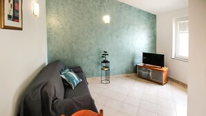 A living room with a sofa, a TV on a cabinet, a small plant, and a wall with a textured finish. - Gorgeous apartment in Stara Novalja with outdoor swimming pool (Stara Novalja)