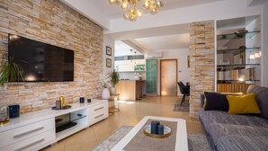 Ein modernes Wohnzimmer mit Steinwand, Flachbildfernseher, weißem Unterhaltungsschrank, grauem Sofa mit gelben Kissen und Couchtisch mit Glasplatte.