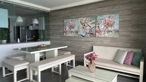 Un salon moderne comprenant un canapé, deux bancs, une table basse et un coin repas avec une table et des chaises en verre.