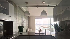 Une cuisine moderne dotée d’un grand îlot central, de luminaires suspendus et offrant une vue sur la mer grâce à de grandes fenêtres.