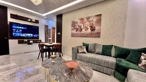 Ein modernes Wohnzimmer mit Flachbildfernseher, Essbereich und einer Couch mit grünen Kissen.