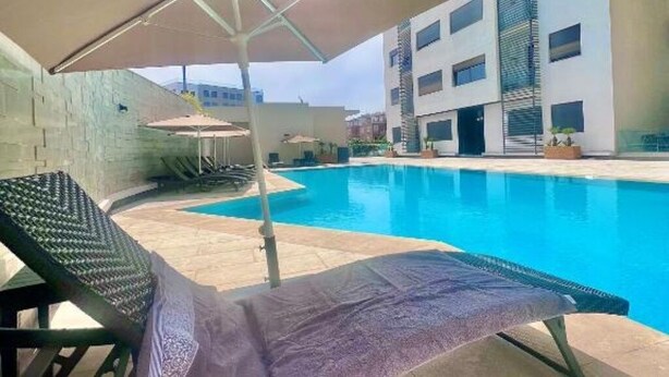 Ein Pool mit Liegestühlen und Sonnenschirmen, umgeben von einem Gebäude mit mehreren Etagen und Balkonen.