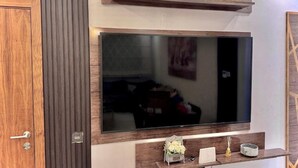Ein modernes Wohnzimmer mit einem großen Flachbildfernseher an einer Holzwand, einer Holztür und einem kleinen Regal mit Dekoration.