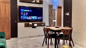 Ein modernes Wohnzimmer mit Wand-Fernseher, einem Holzesstisch mit Stühlen und einem grünen Sofa.