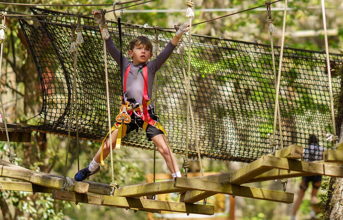 Eine Person überquert eine Seilbrücke, gesichert durch Sicherheitsgurte und Seile.
