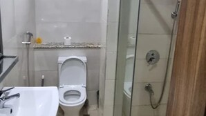 Egy fürdőszoba üvegfalas zuhanyzóval, WC-vel és mosdókagylóval.