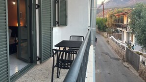 Een balkon met een tafel en stoelen, uitzicht op een bergketen en een straat met een hek en een gebouw met een balkon.