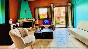 A living room with a fireplace, a television, a sofa, and a chair. - Anemeli 2 bedroom Apartment, Stoupa, 50m to beach. Stunning Sea & Mountain views (Stoupa)