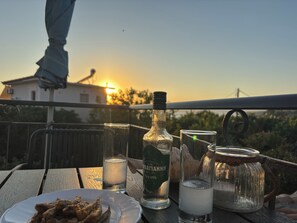 A table with a plate of fried food, a bottle of liquor, and glasses, set against a sunset backdrop. - Anemeli 2 bedroom Apartment, Stoupa, 50m to beach. Stunning Sea & Mountain views (Stoupa)