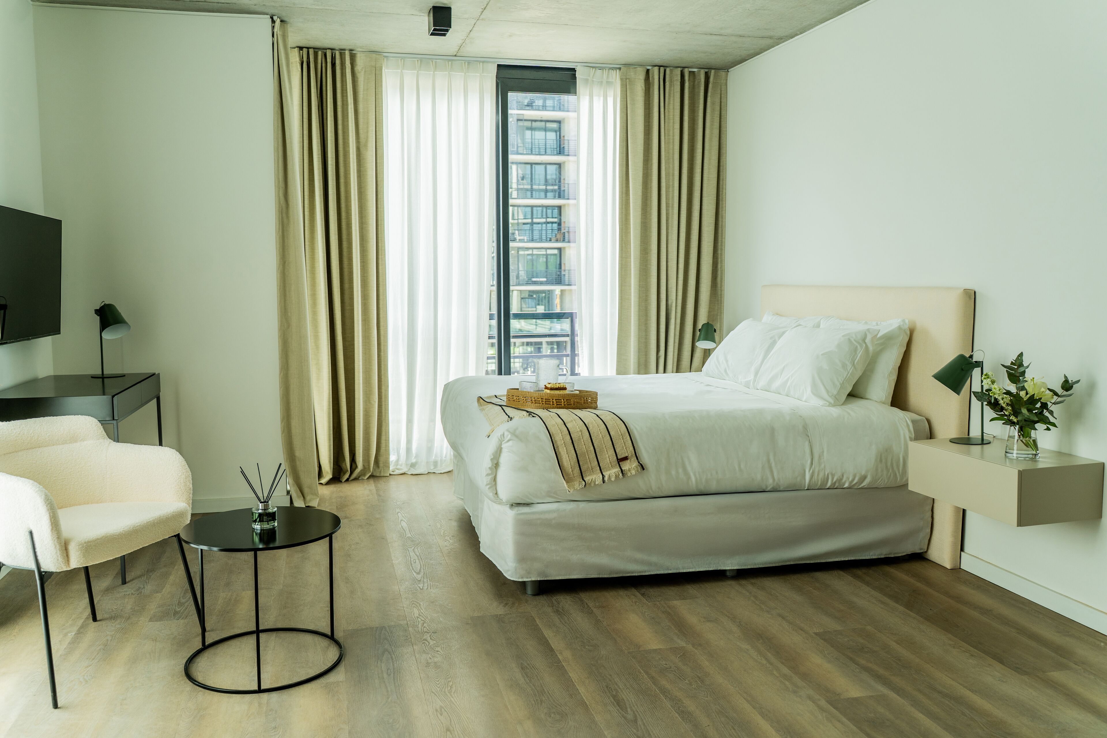 A modern hotel room with a bed, a chair, a small table, and a TV.