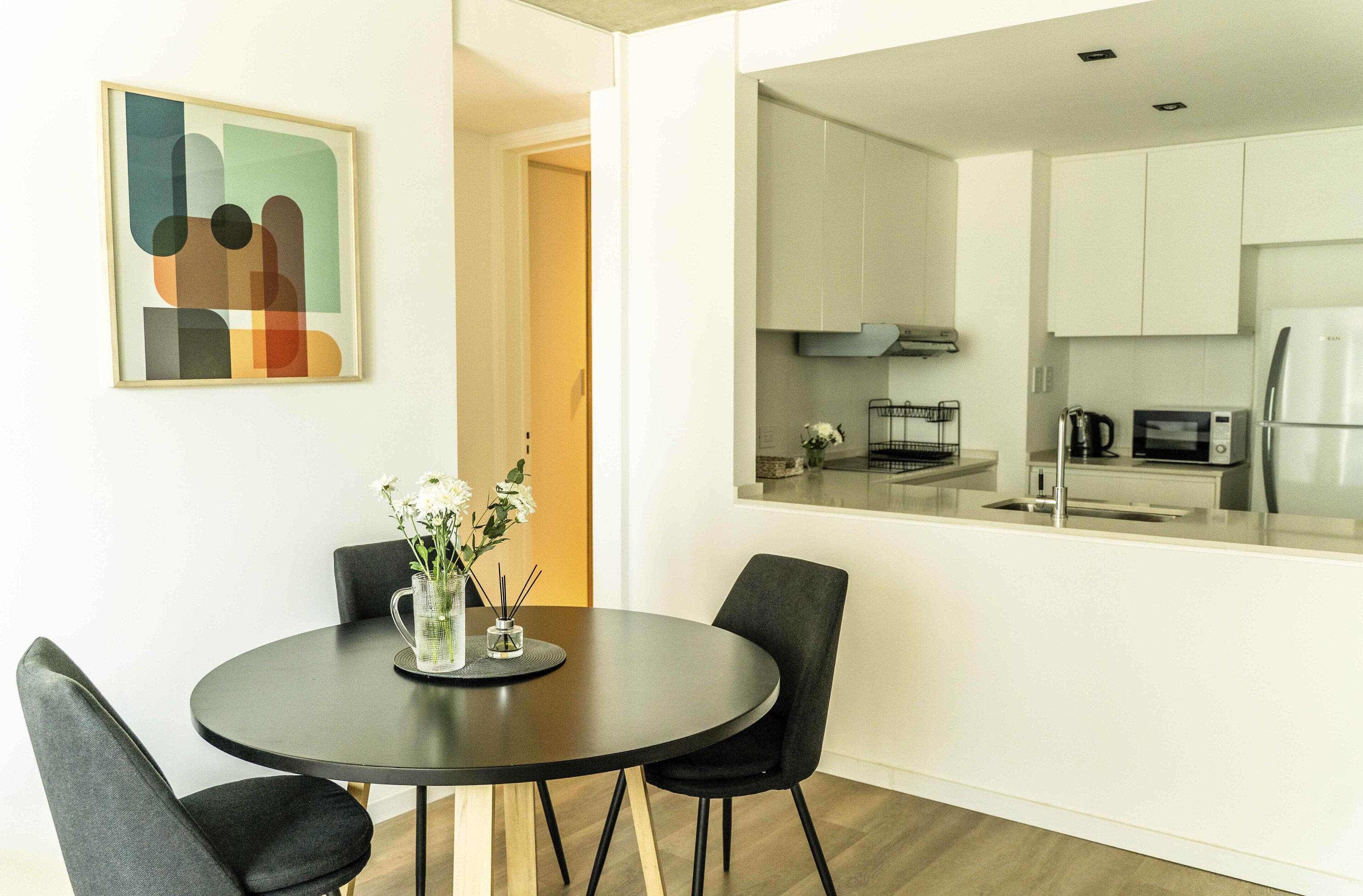 A modern dining area with a round table, black chairs, and a vase with flowers.
