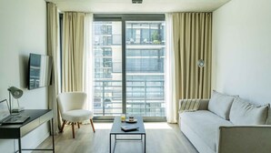 Una sala de estar moderna con sofá, mesa de centro, una silla, escritorio con computadora portátil y un ventanal con cortinas.