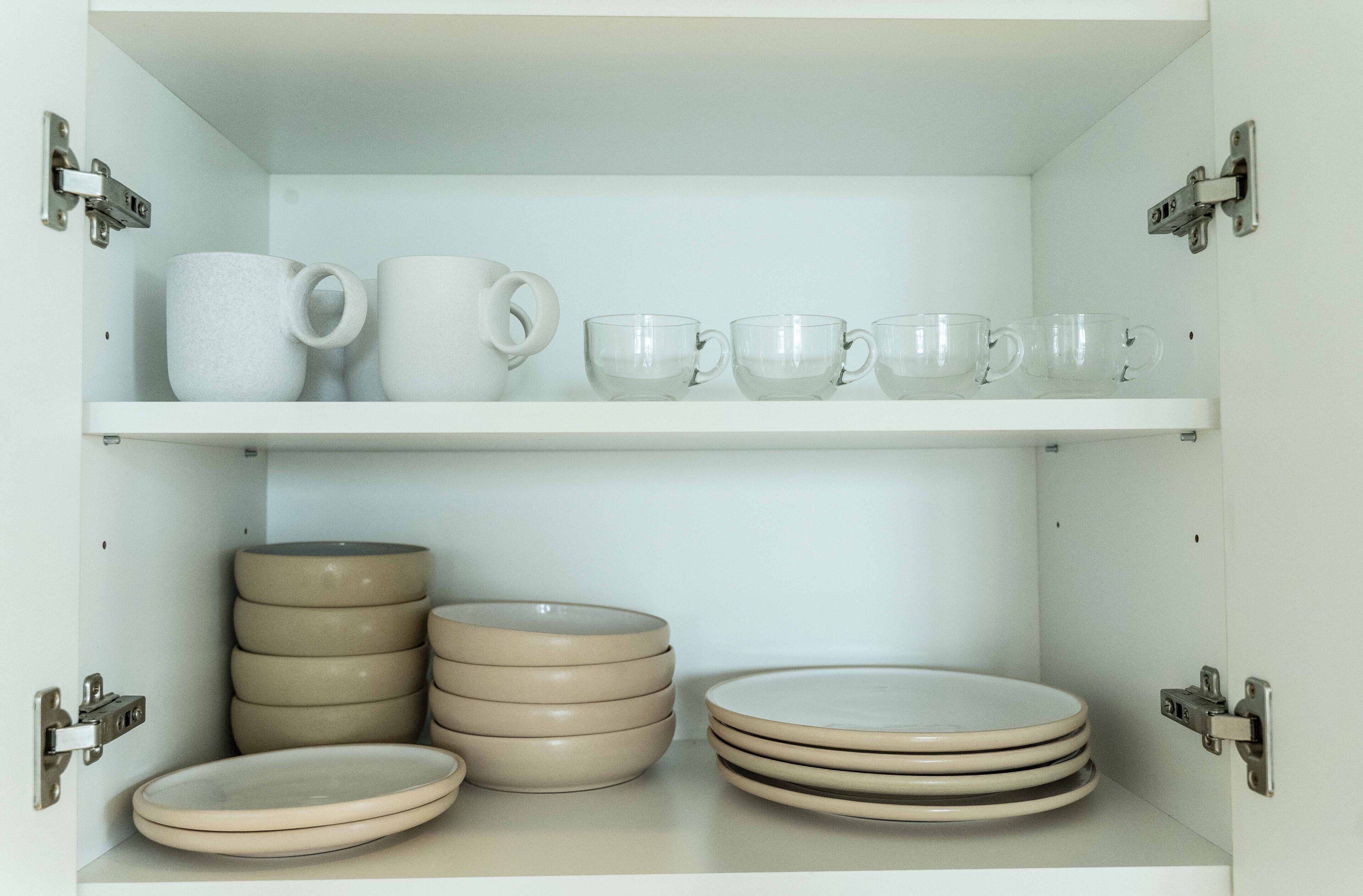 A storage cabinet with shelves holding plates, bowls, and cups.