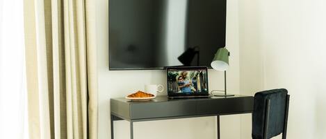A modern room with a flat-screen TV mounted on the wall, a desk with a laptop, a lamp, and a chair.