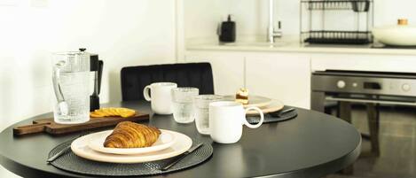 A breakfast setting with a croissant, coffee cups, and a teapot on a round table.
