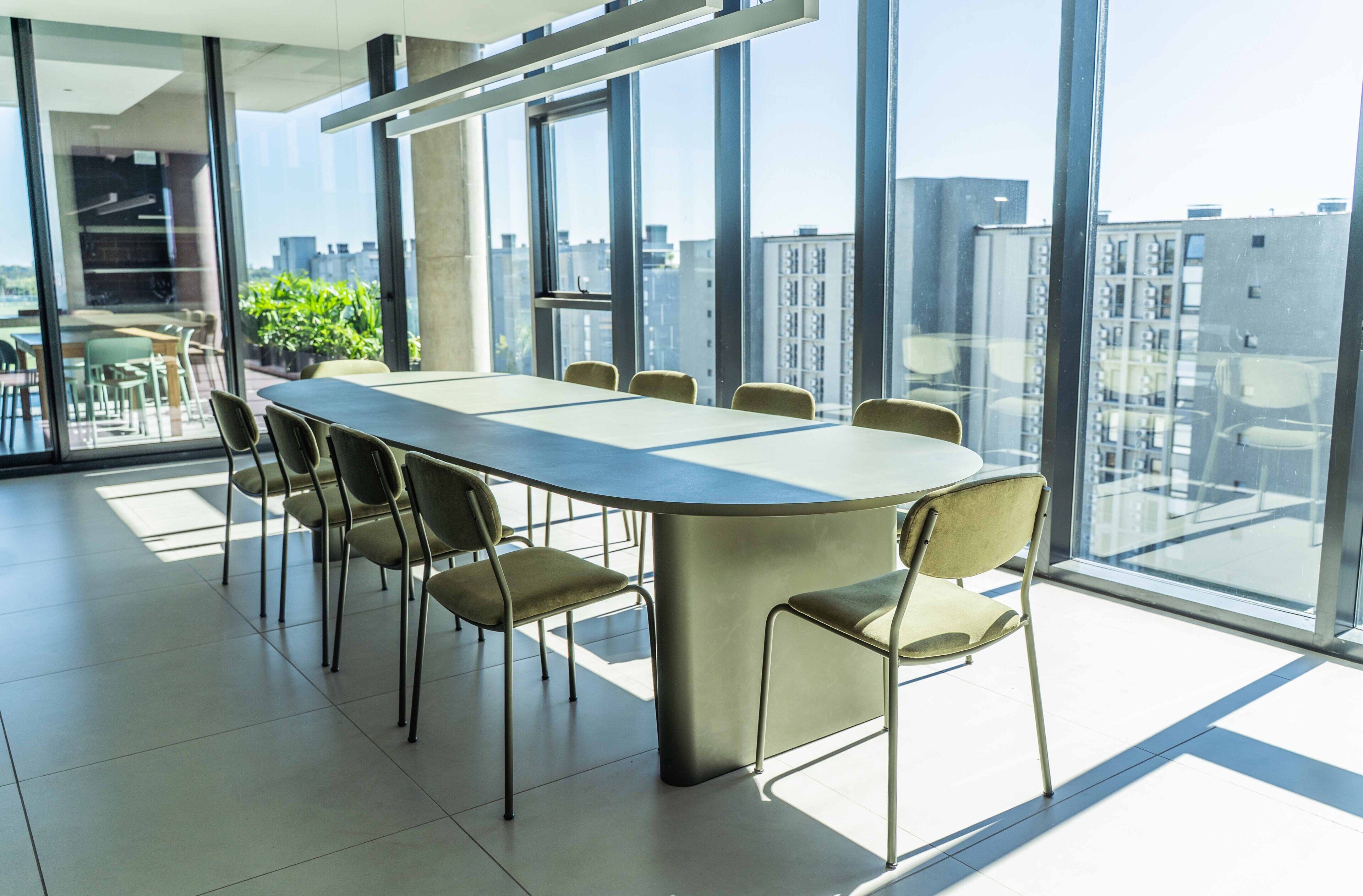 A modern conference room with a long table and chairs, large windows with a city view, and a tiled floor.