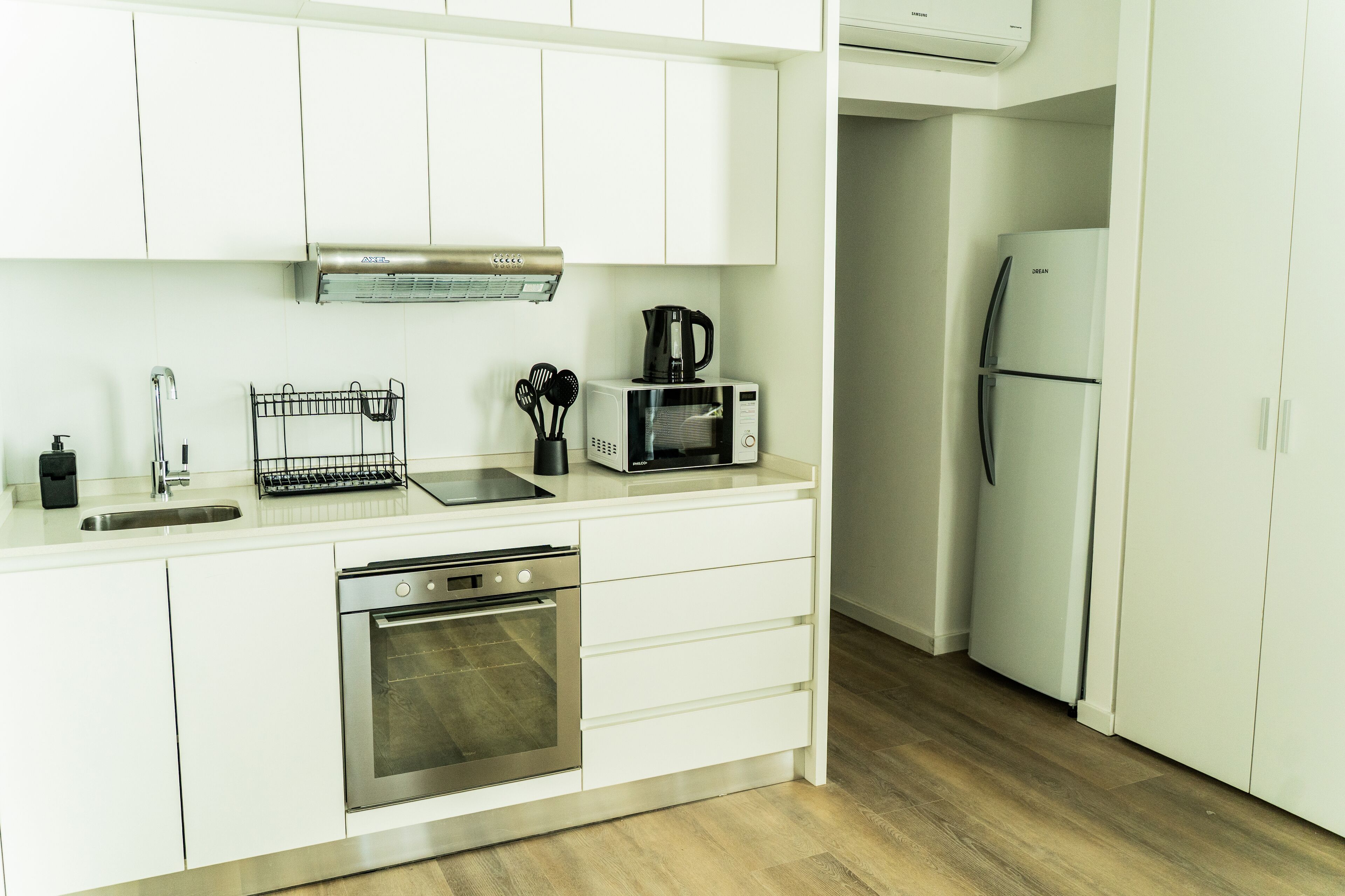 A modern kitchen with white cabinets, stainless steel appliances, a microwave, a coffee maker, and a refrigerator.
