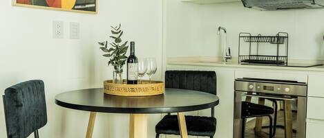 Una cocina moderna con gabinetes blancos, horno empotrado y comedor con una mesa redonda y sillas negras.