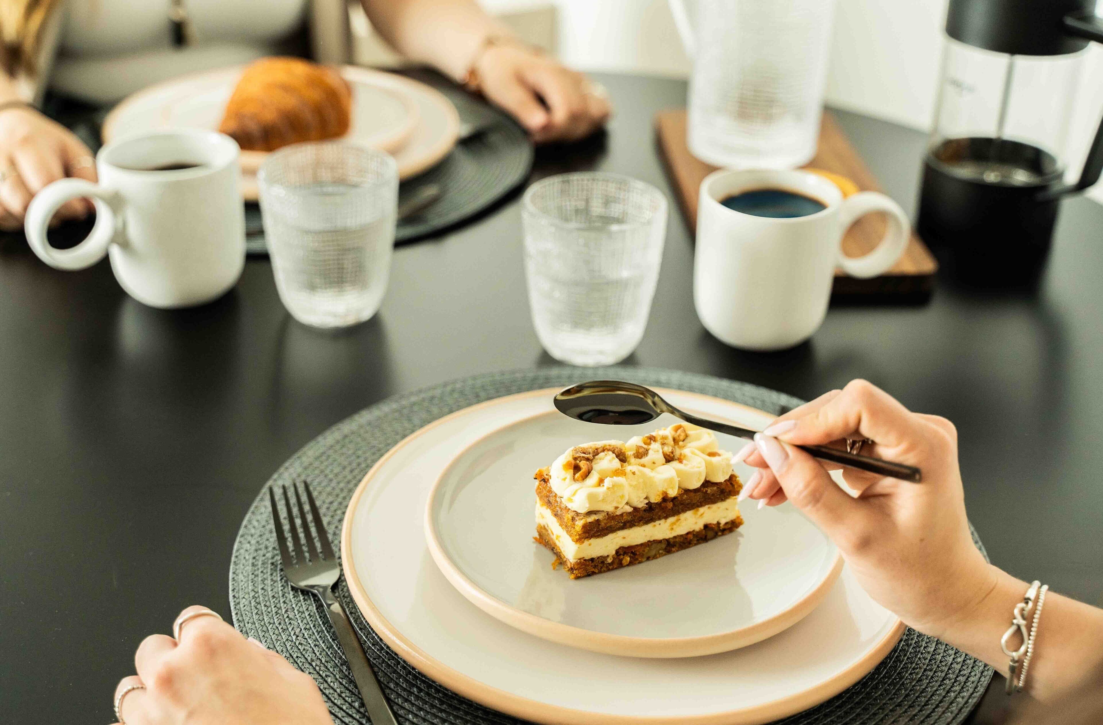 Una mesa de comedor con un plato de pastel, una taza de café y un vaso de agua.