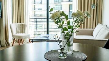 Una sala de estar moderna con una mesa redonda, un florero con flores y vistas a un paisaje urbano a través de amplios ventanales.