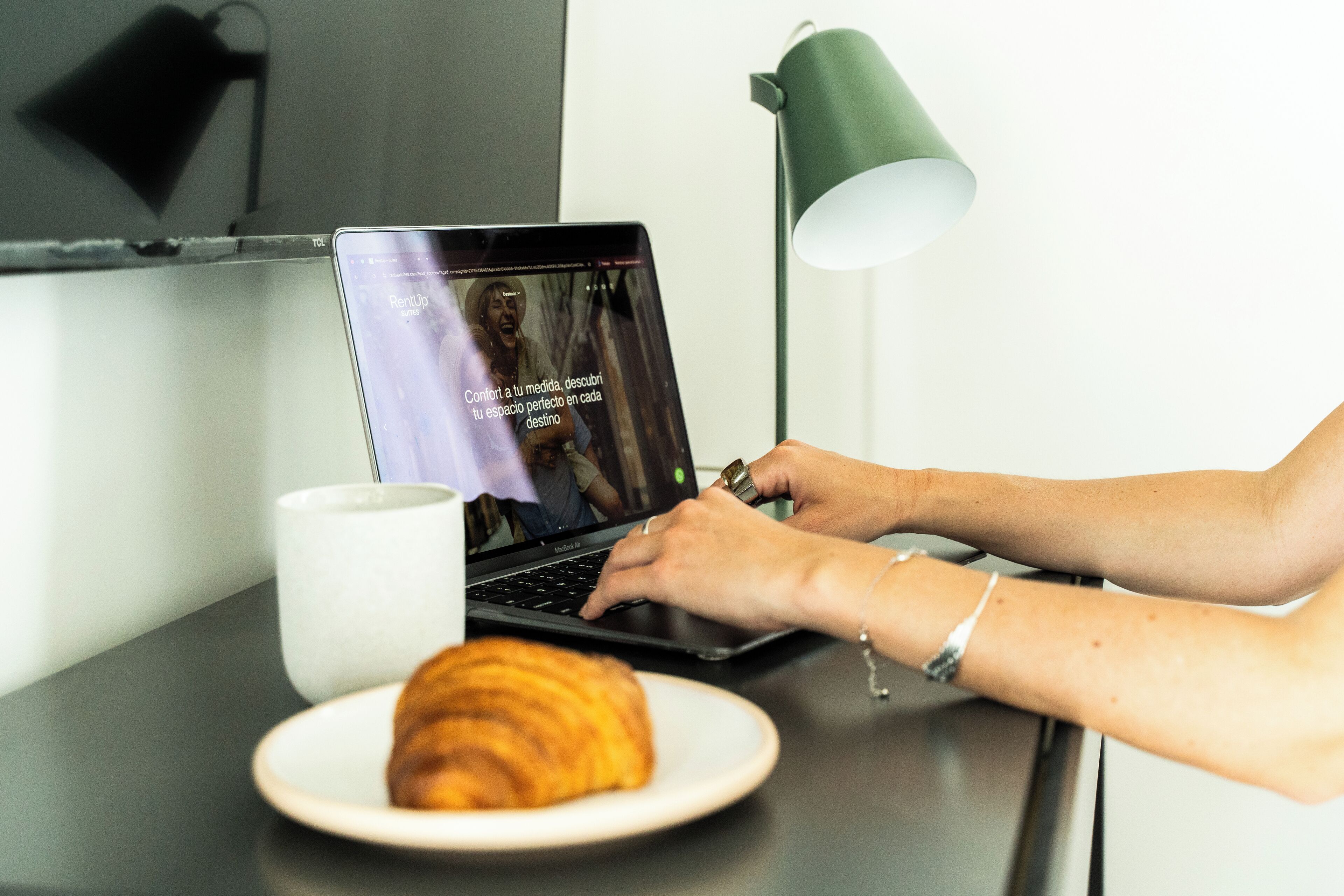 A laptop on a desk with a croissant and a mug.
