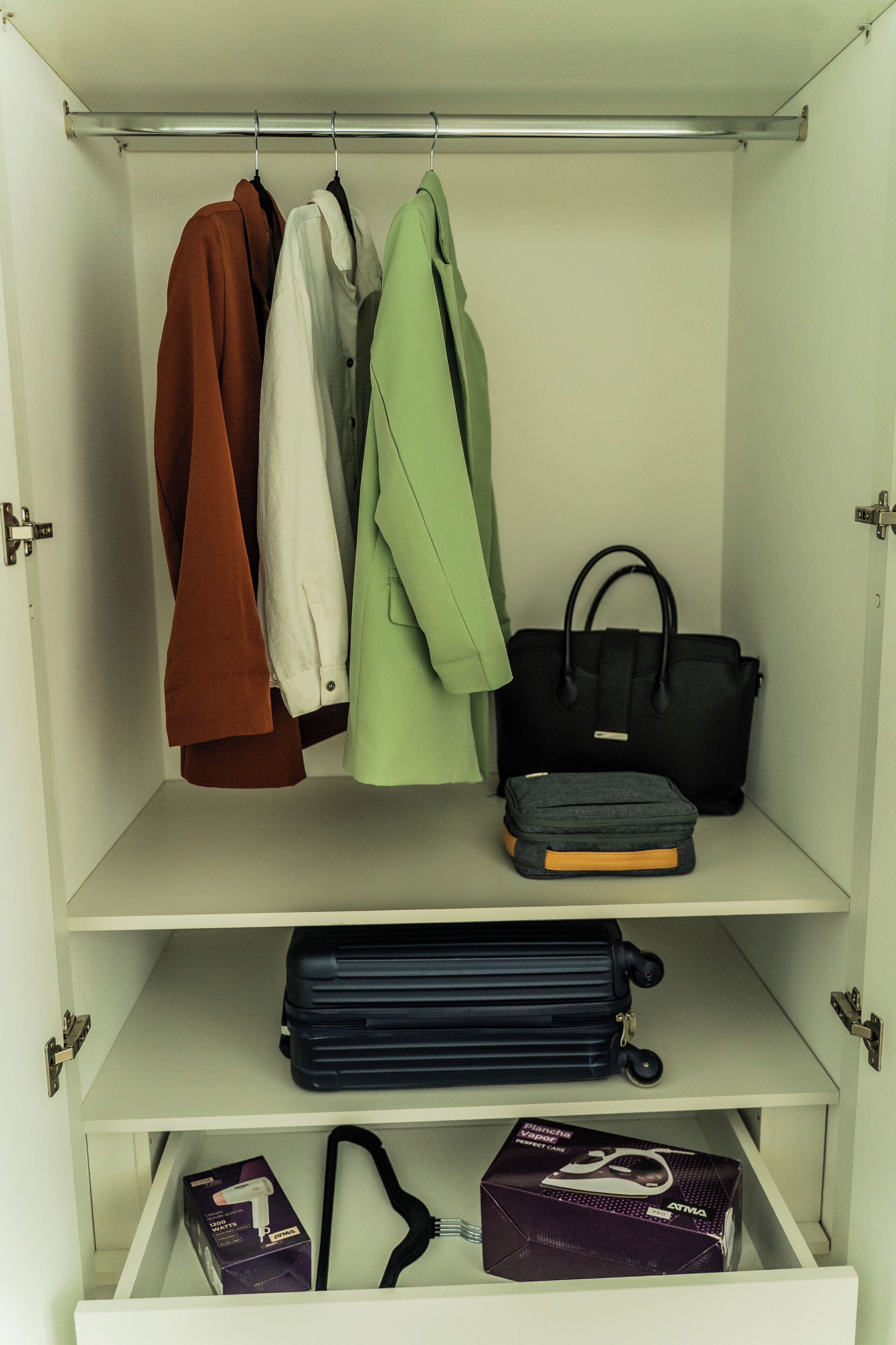 A wardrobe with hanging clothes, a handbag, and storage boxes.