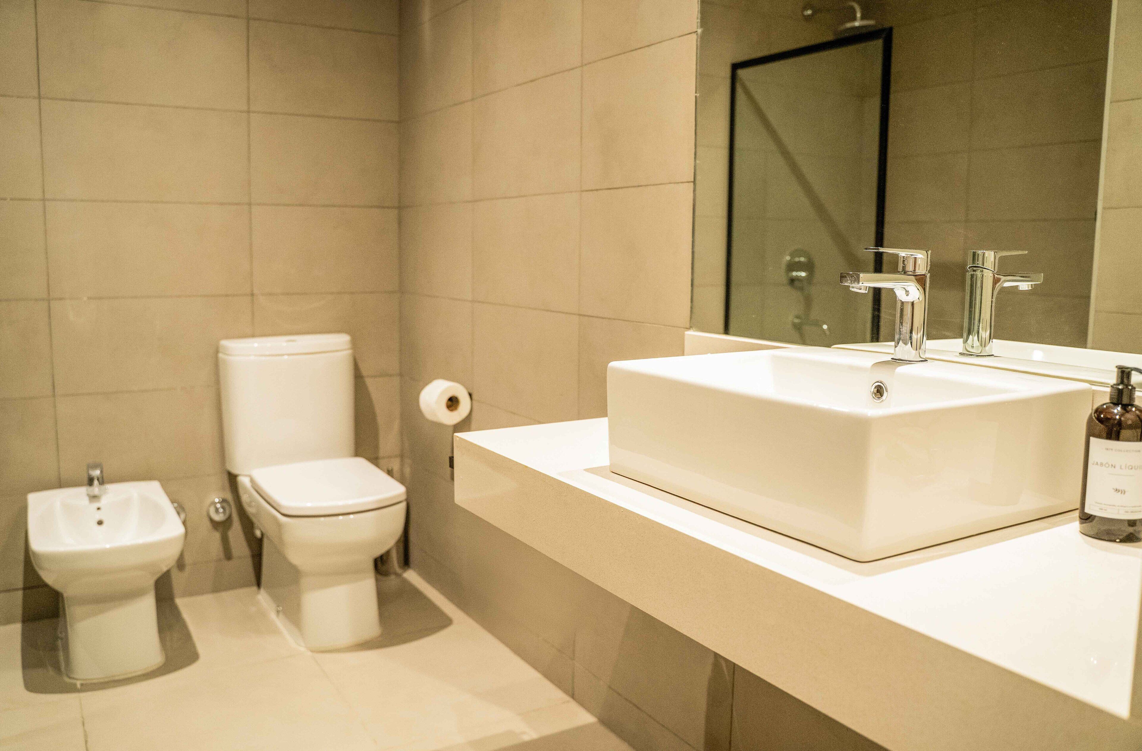 A bathroom with a bidet, toilet, and a large sink with a mirror above it.