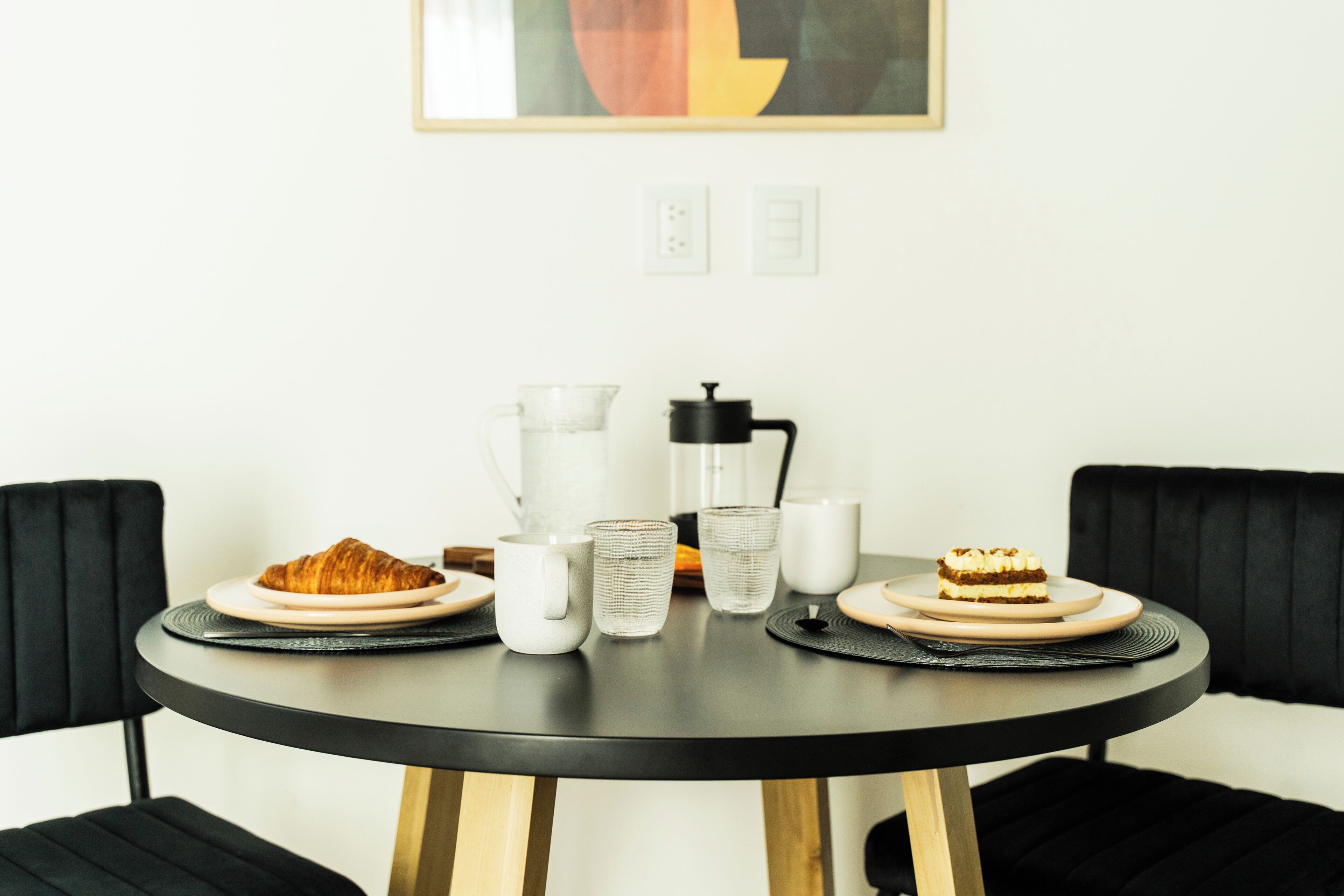 Una mesa redonda con platos de comida, tazas y una cafetera.