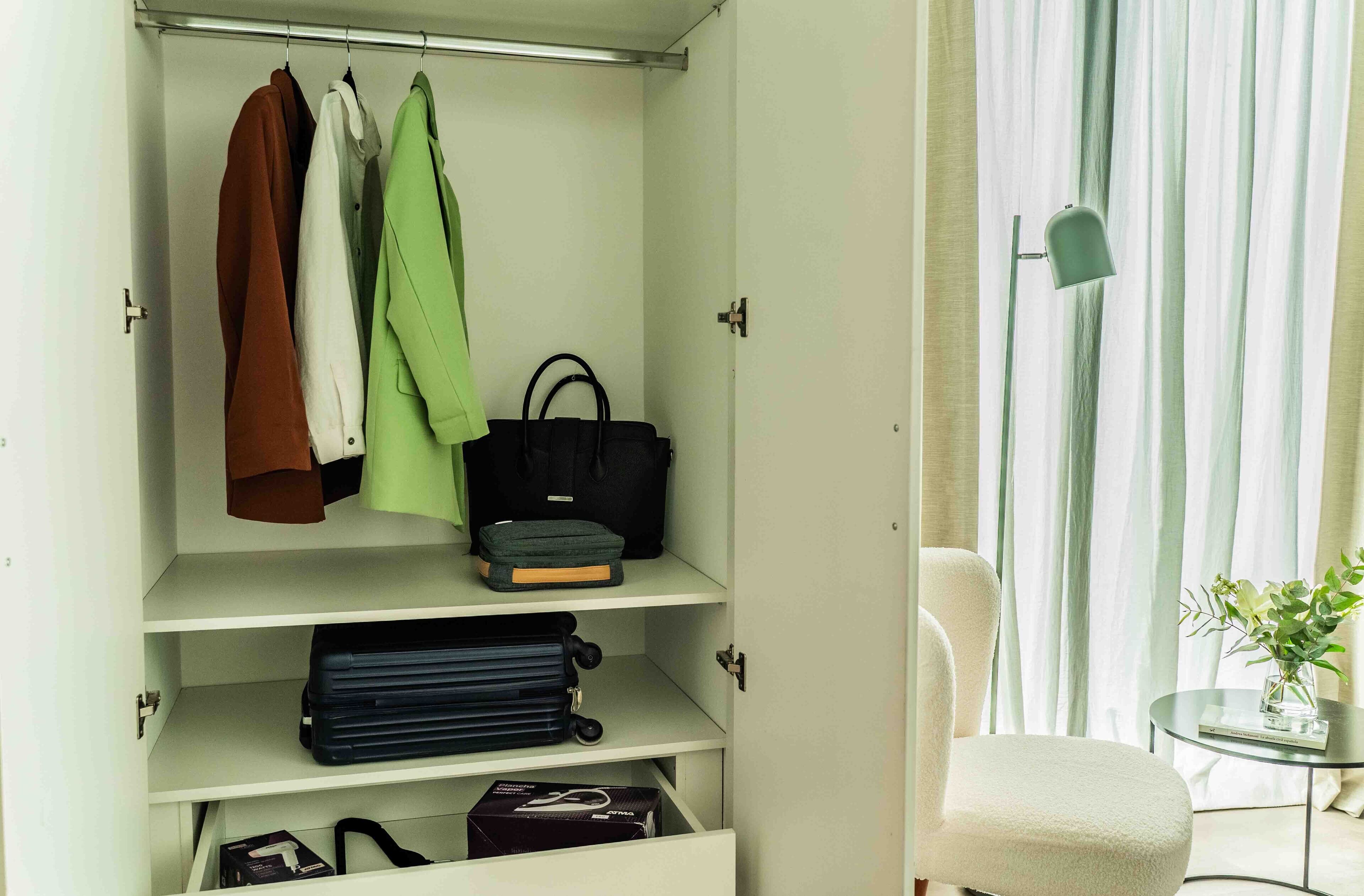 A neatly organized wardrobe with hanging clothes and shelves containing bags and boxes.