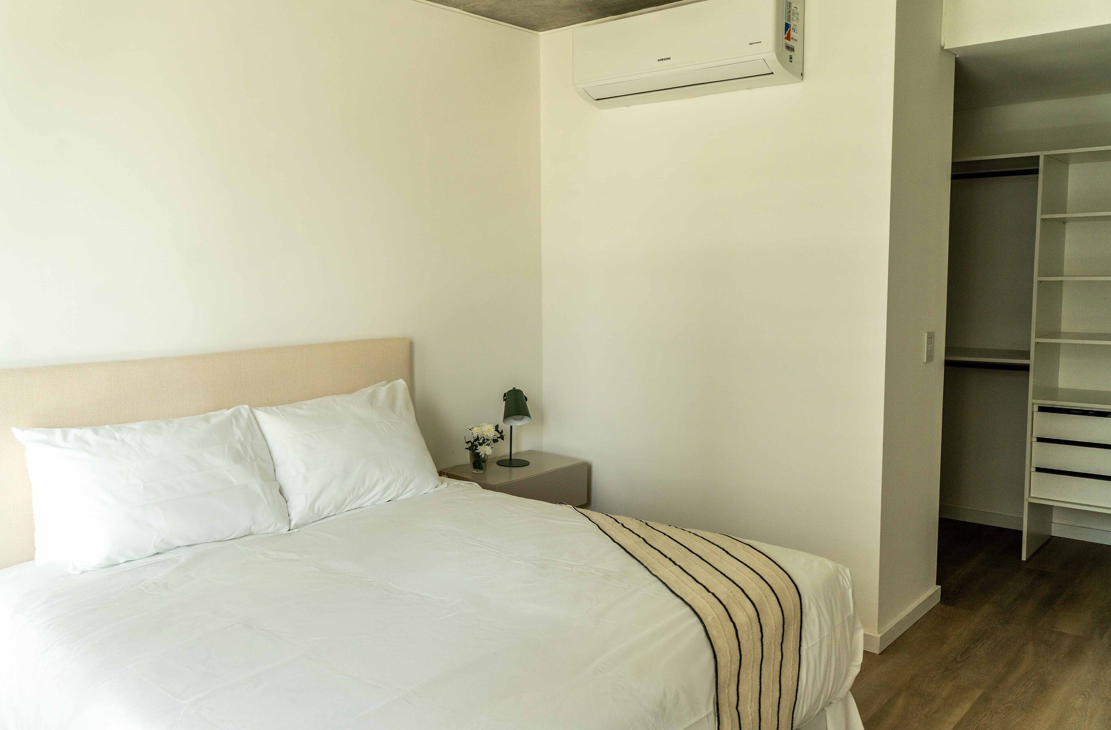 Une chambre d’hôtel comprenant un lit, une table de chevet, une lampe, un appareil de climatisation et un placard.