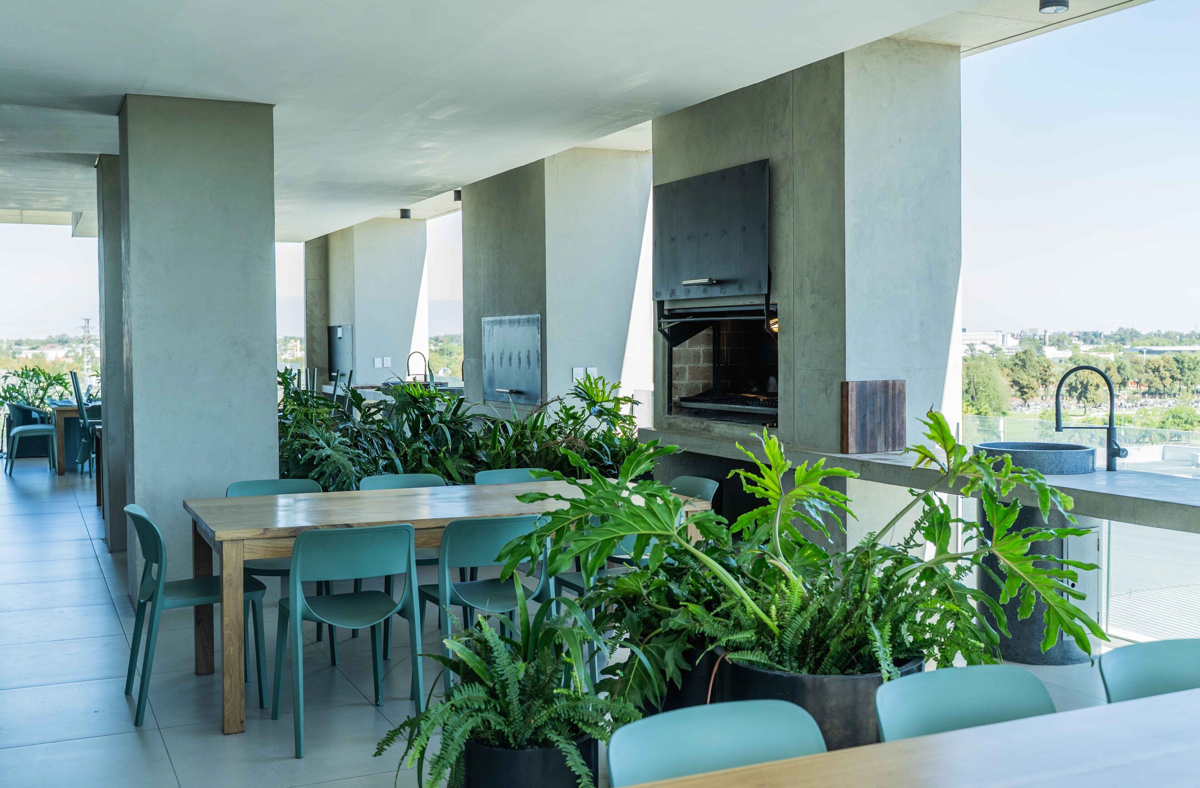 An outdoor dining area with tables and chairs, a built-in grill, and potted plants.