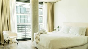 Habitación de hotel con una cama grande, una silla, una ventana con cortinas y vistas a edificios.