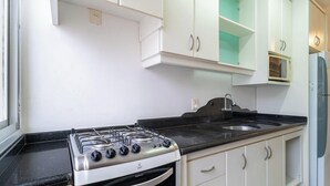 A kitchen with white cabinets, a gas stove, a sink, and a microwave. - Apt 3 Bedrooms in Floripa Downtown Idr0801 (Florianópolis)